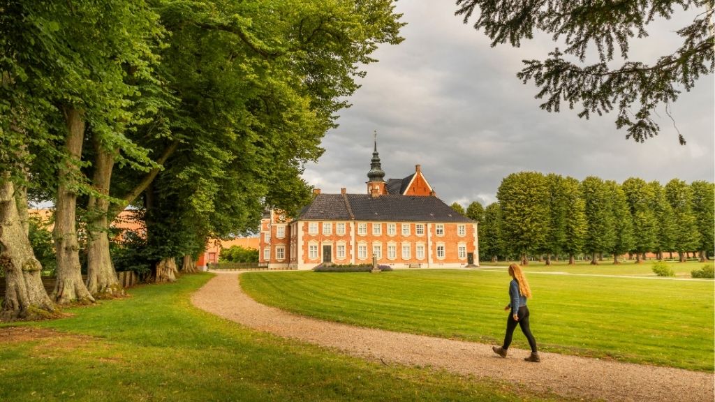 Jægerspris Castle seen from the park with a visitor walking in the foreground.