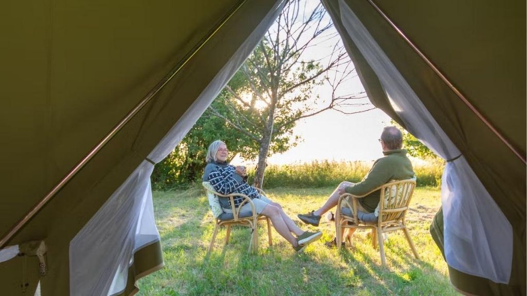 Two people sit outside a glamping tent at Snoremark, seen through the tent entrance.