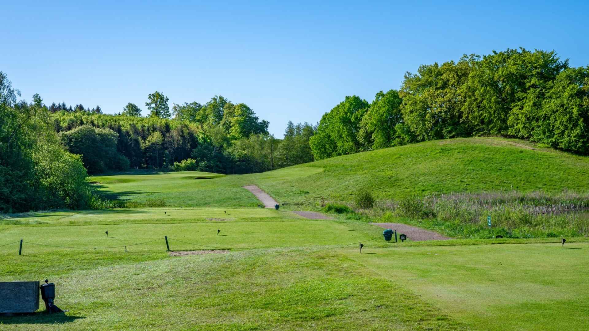 Golf course at Ledreborg Palace Golf Club surrounded by green hills and forest.