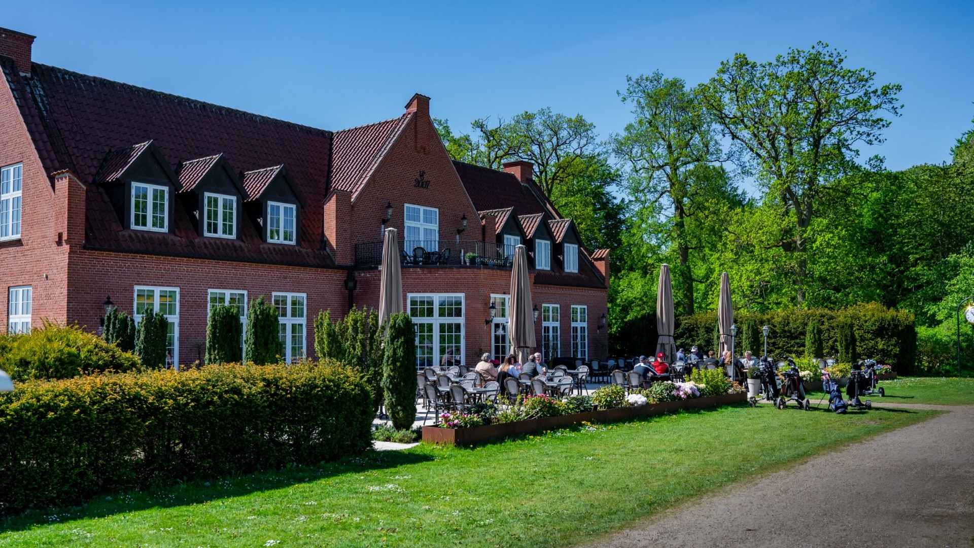Guests sitting on the terrace in front of Ledreborg Palace Golf Club’s clubhouse.