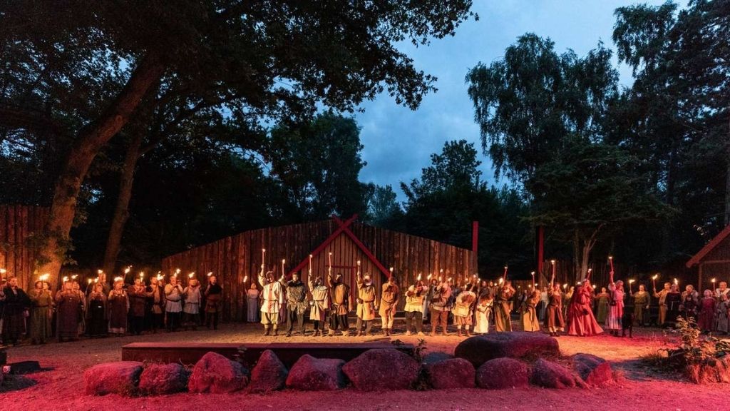 Evening performance at Frederikssund Viking Play with actors in Viking costumes holding torches in front of the stage.