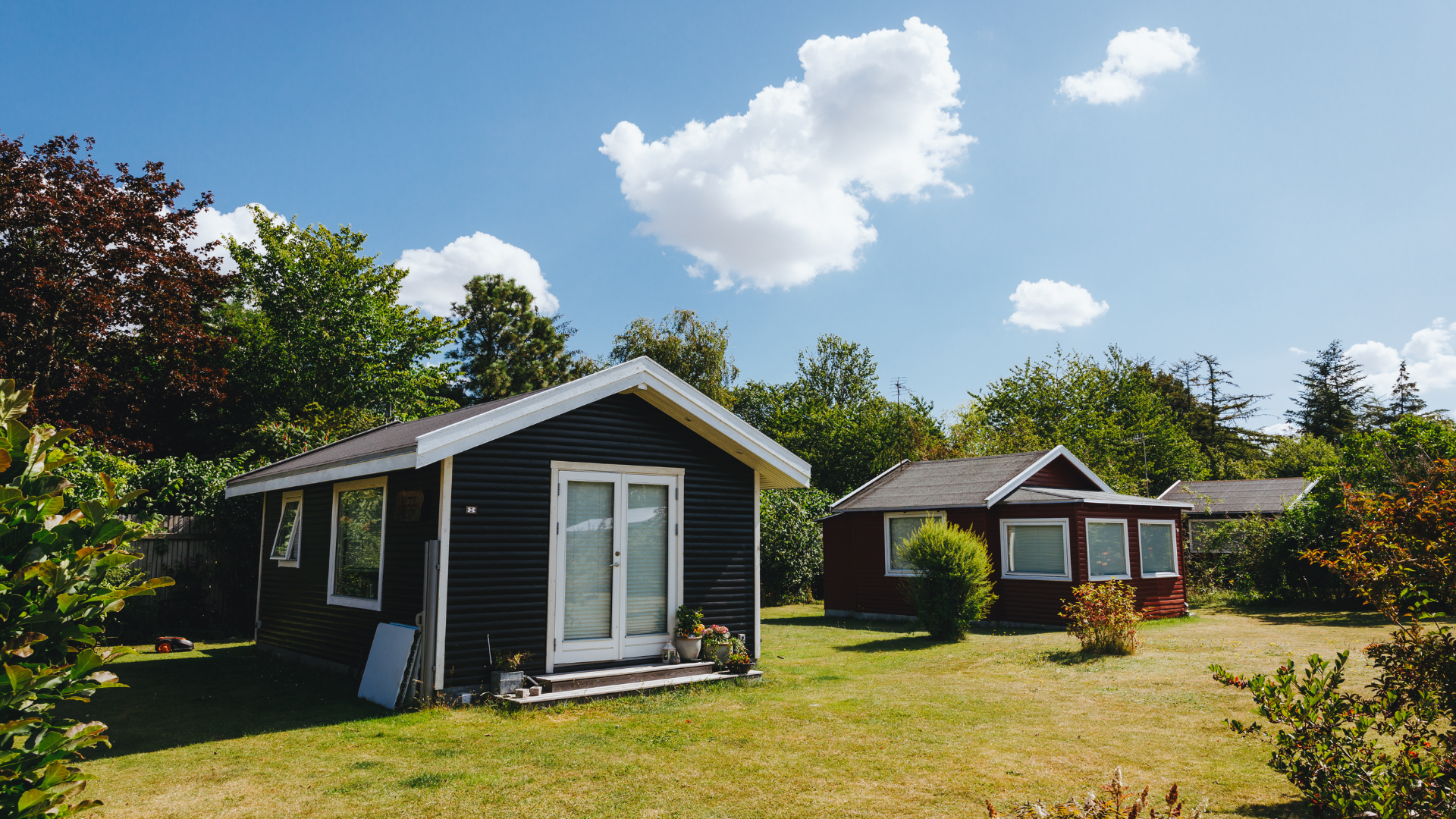 Holiday cabins in green surroundings with lawn, trees and blue sky.