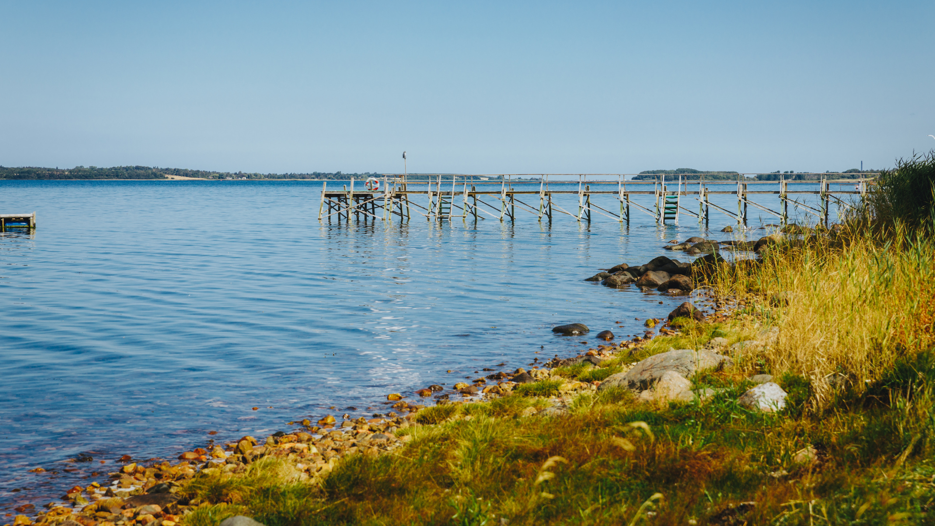 Bathing jetty at Solbakken Camping with calm water, shoreline stones and green vegetation.