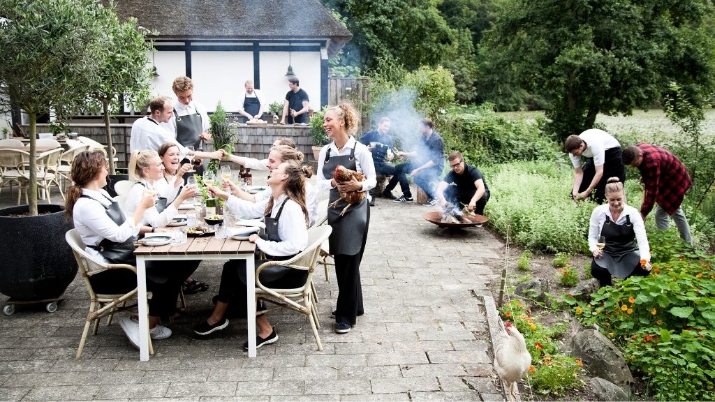 Udendørs servering og køkkenhave ved Restaurant Herthadalen med gæster og personale.