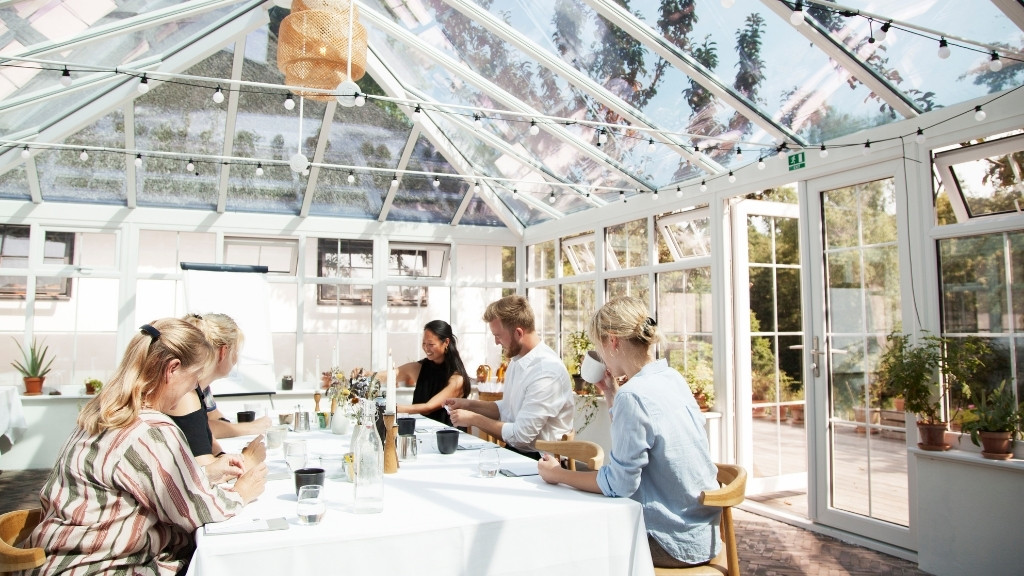 Gæster samlet omkring bord i orangeriet hos Restaurant Herthadalen.