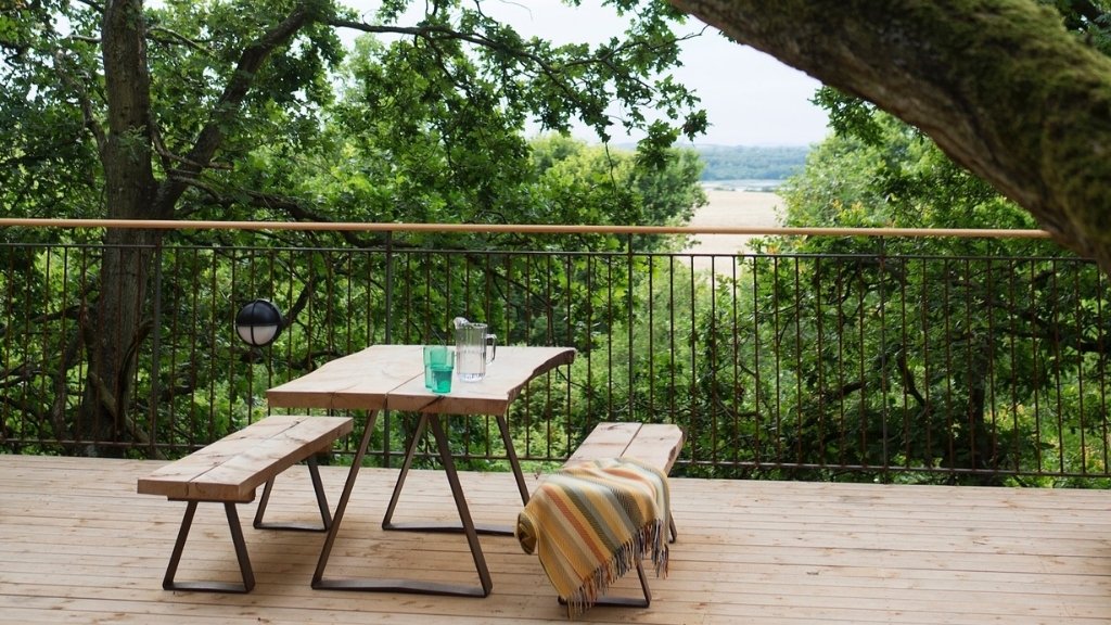 Terrasse ved trætophytterne på Ryegaard Gods med bord og udsigt over naturen.