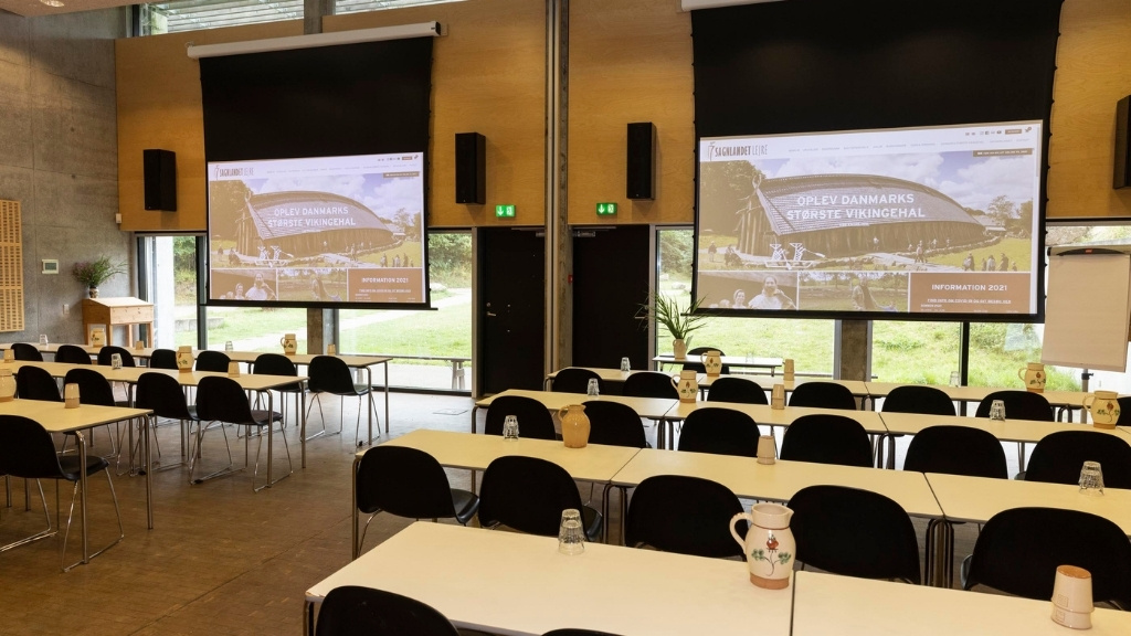 Konferencesal i Sagnlandet Lejre med borde, stole og store lærreder.