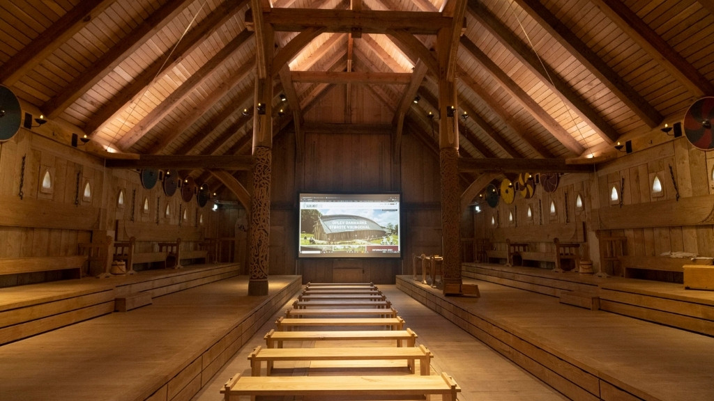 Kongehallen i Sagnlandet Lejre med træbænke, udskårne søjler og højt loft.