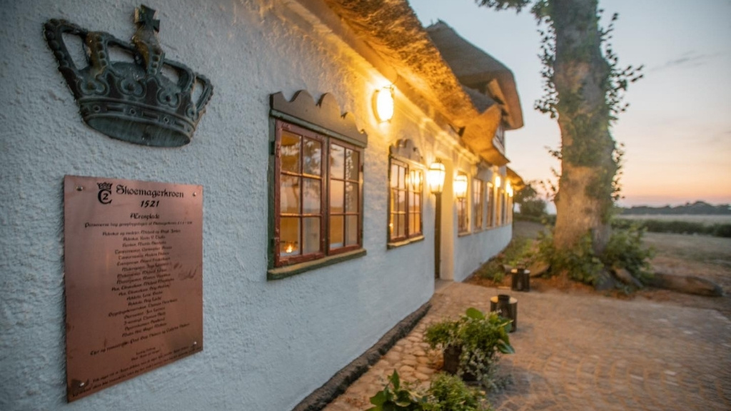 Historisk facade på Skovmagerkroen med oplyste vinduer i aftentimerne.