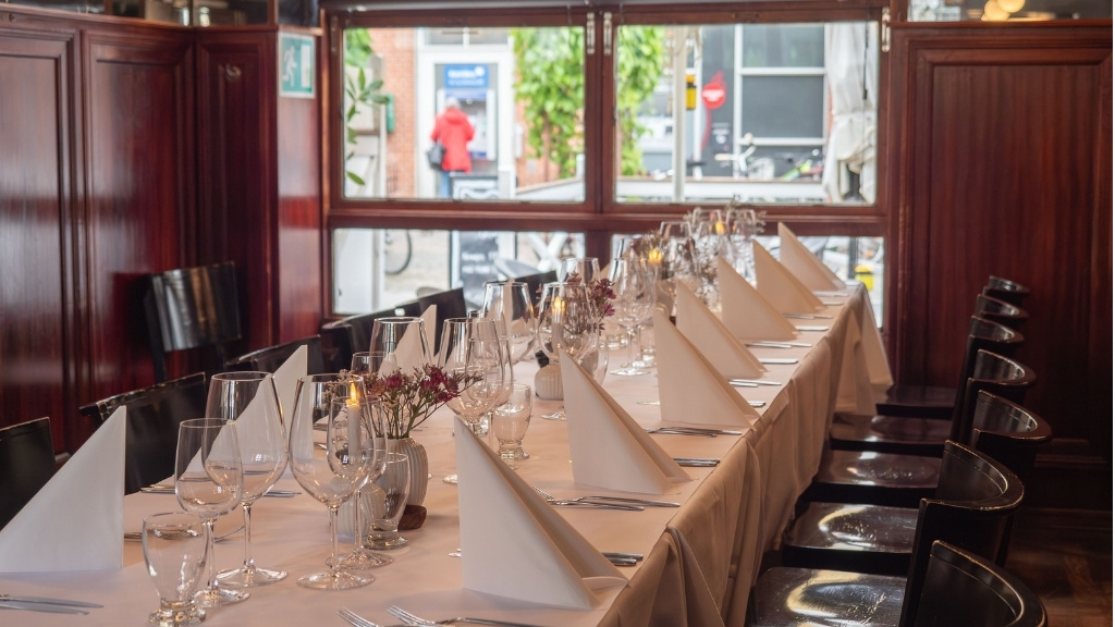 Opdækning i spisestuen hos Restaurant Bryggergården med langborde og hvide duge.