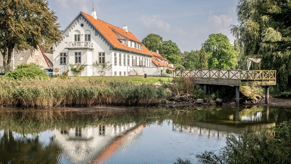 Main building of Sonnerupgaard Gods by the water surrounded by greenery.