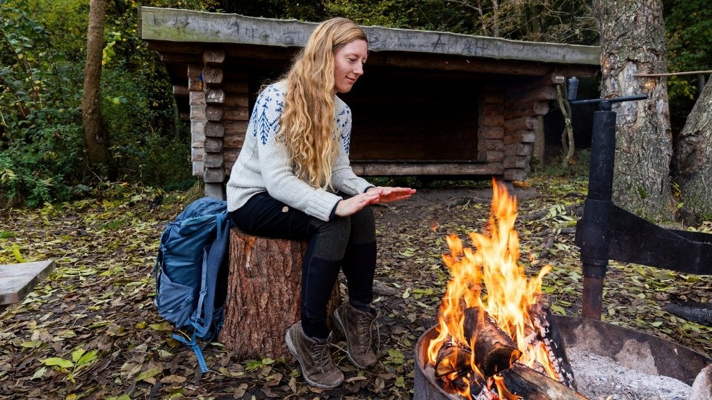 Person sitting by a campfire at Kong Roars shelter in Boserup Forest.