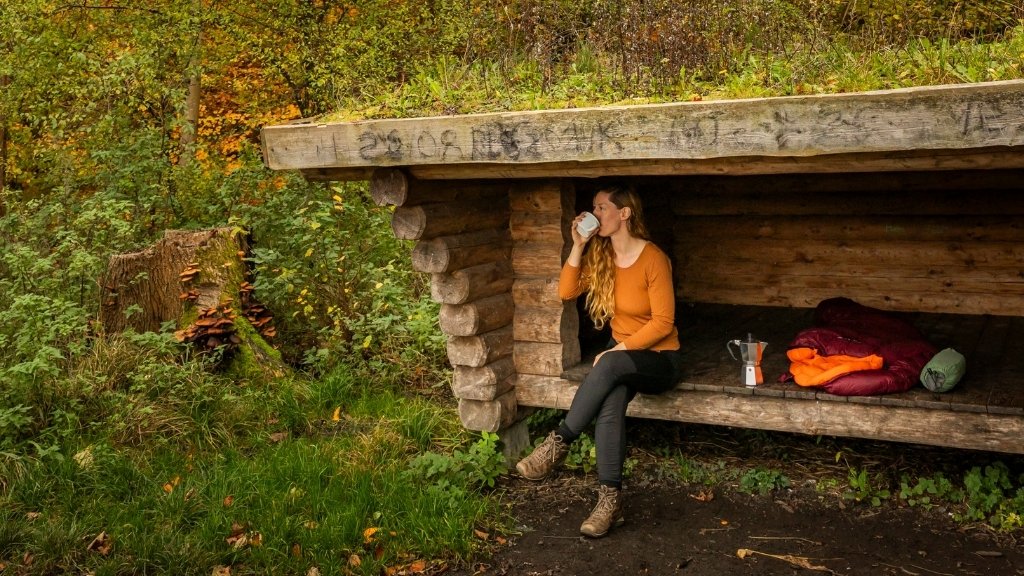 Woman sitting in Kong Roars shelter in Boserup Forest with backpack and outdoor gear.