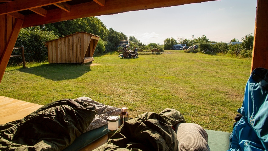 Shelterovernatning på DCU Camping Kulhuse med udsigt til grønne arealer og picnicborde.