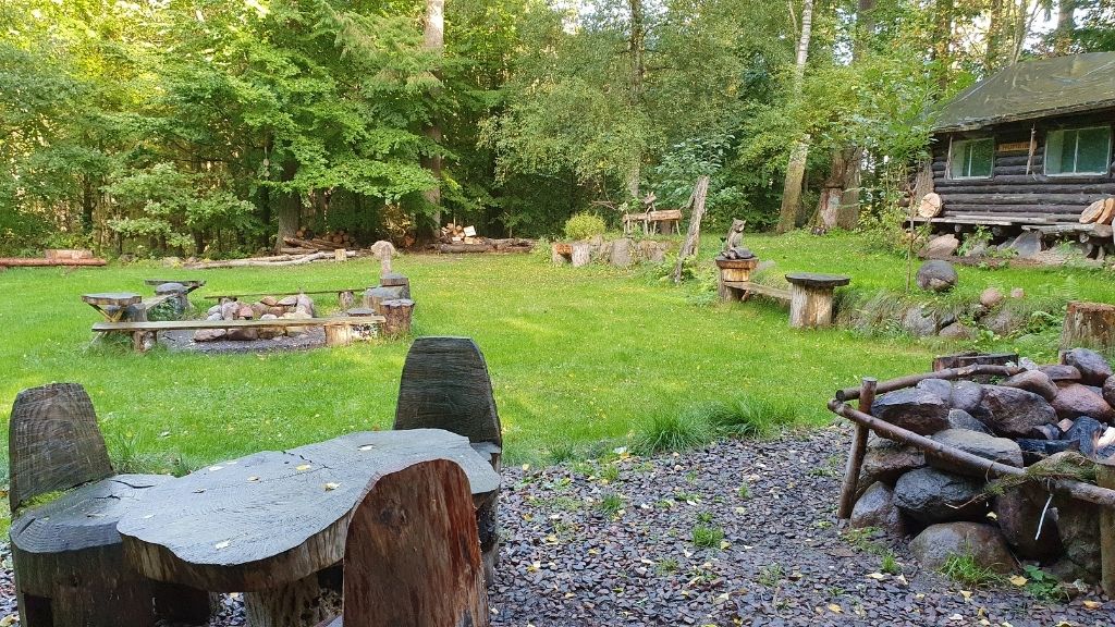 Grøn lejrplads med bålsteder og træmøbler ved Friluftsladens shelters.