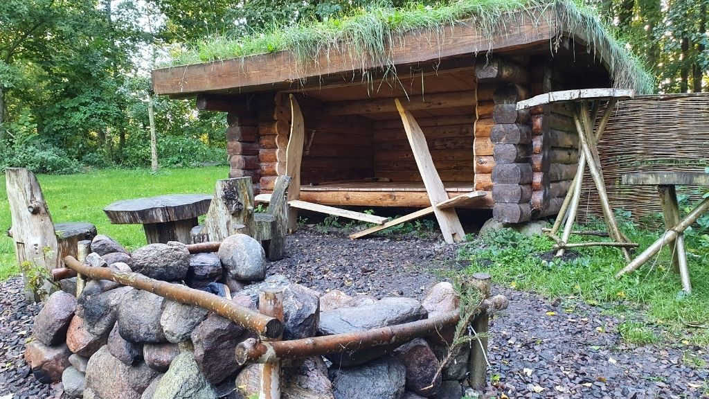 Træshelter med græstag og bålplads ved Friluftsladen.