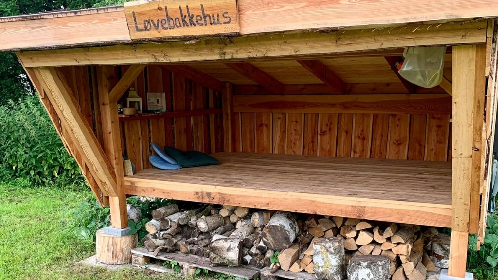 Træshelter ved Løvebakkehus med soveplads og brændeopbevaring.