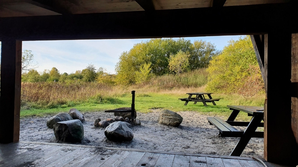 Blick aus dem Shelter Bifrost im Sillebro Ådal auf Feuerstelle und Natur.