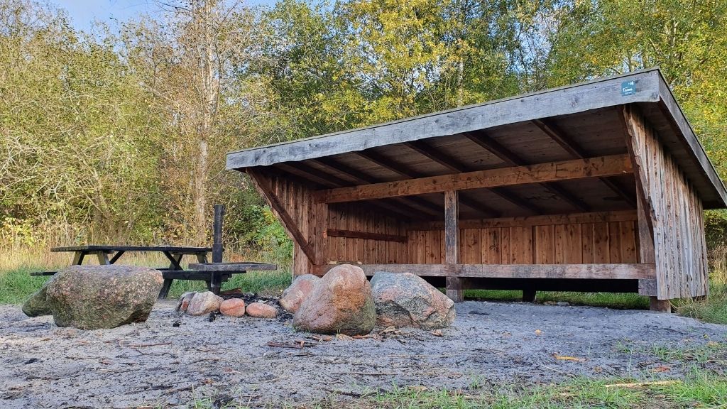 Shelter Bifrost im Sillebro Ådal mit Feuerstelle, Steinen und Picknicktisch.
