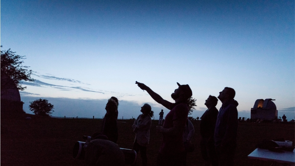 Gruppe af mennesker til stjernekiggeraften ved observatoriet i skumringen.