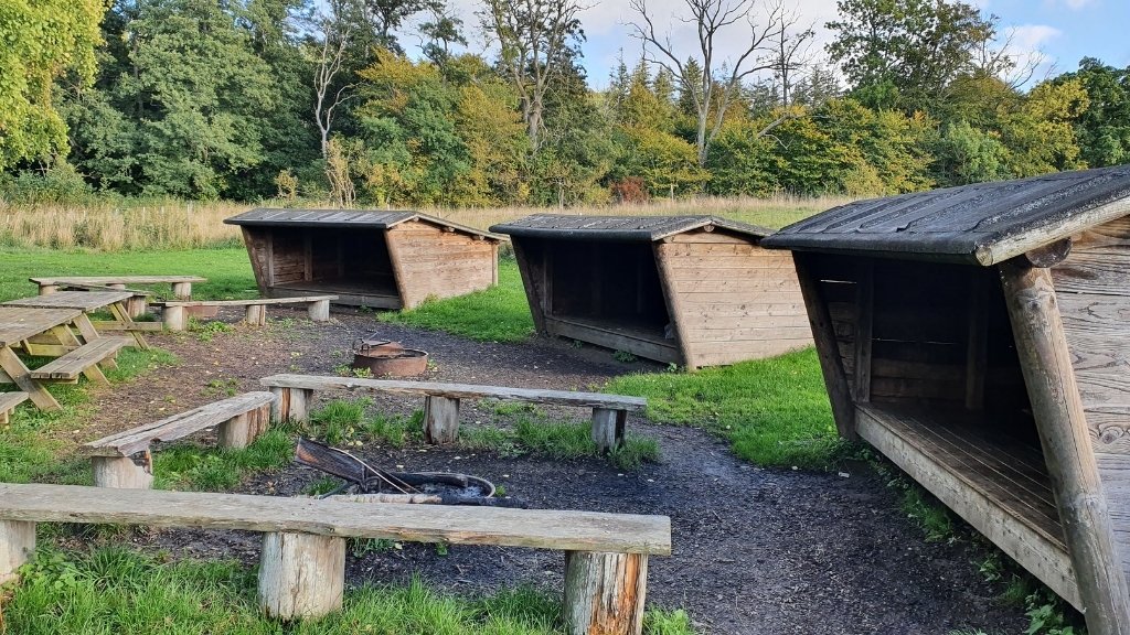 Shelters und Feuerstelle auf dem Tadre Mølle Lagerplatz, umgeben von Wald und Grünflächen.