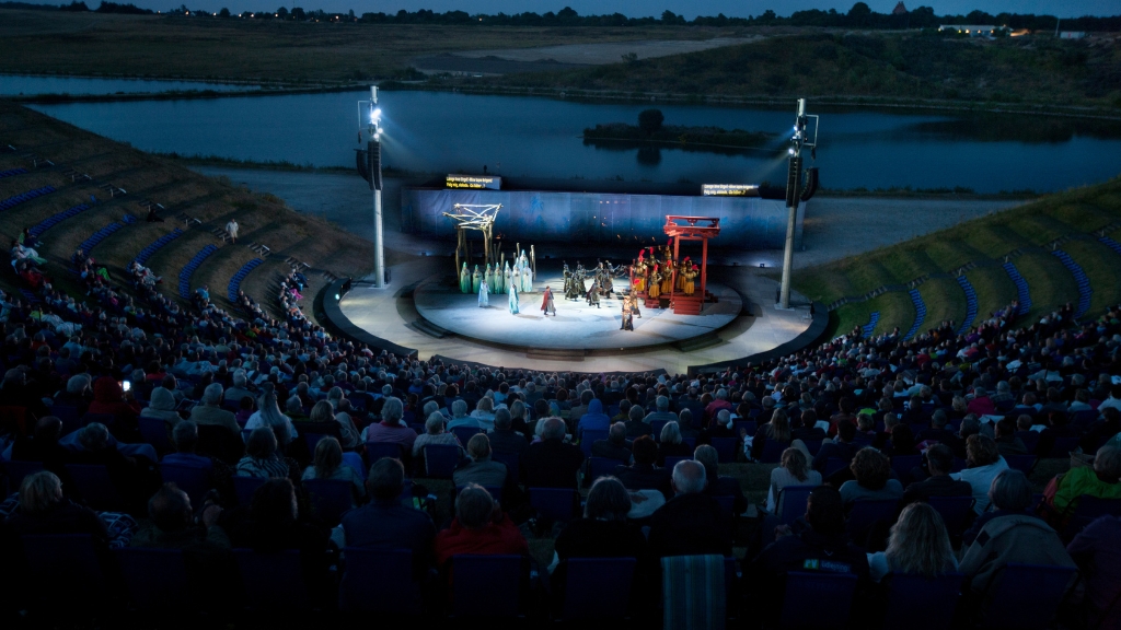 Opera performance at Opera Hedeland with illuminated stage and a full outdoor amphitheatre by the lake.