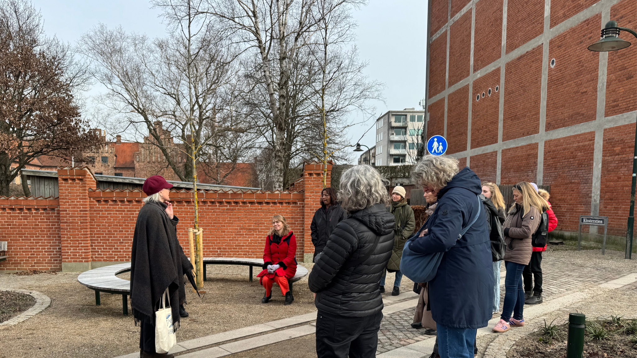 City walk in Roskilde by a historic brick wall with guide and participants.
