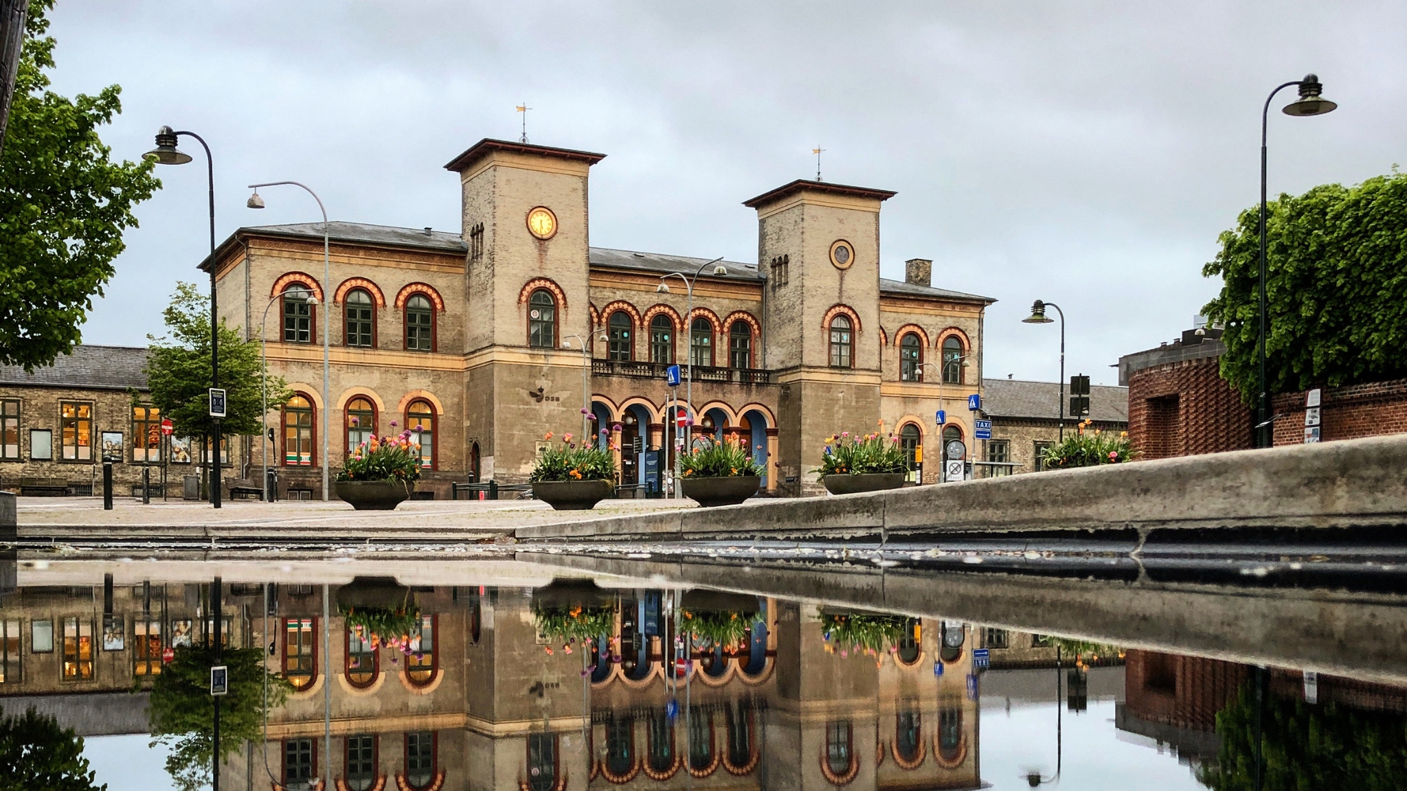 Roskilde Station with facade reflected in a puddle in front of the building.