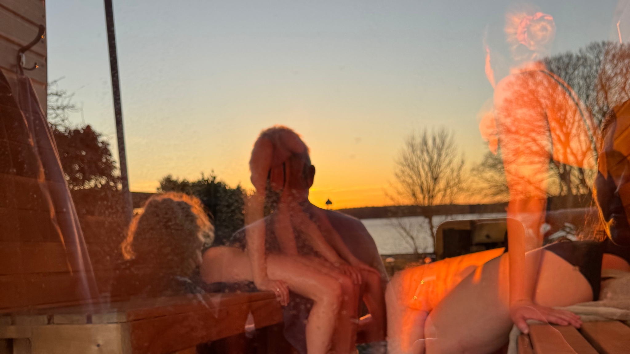 People enjoying a sauna with a sunset view over the water in Frederikssund.