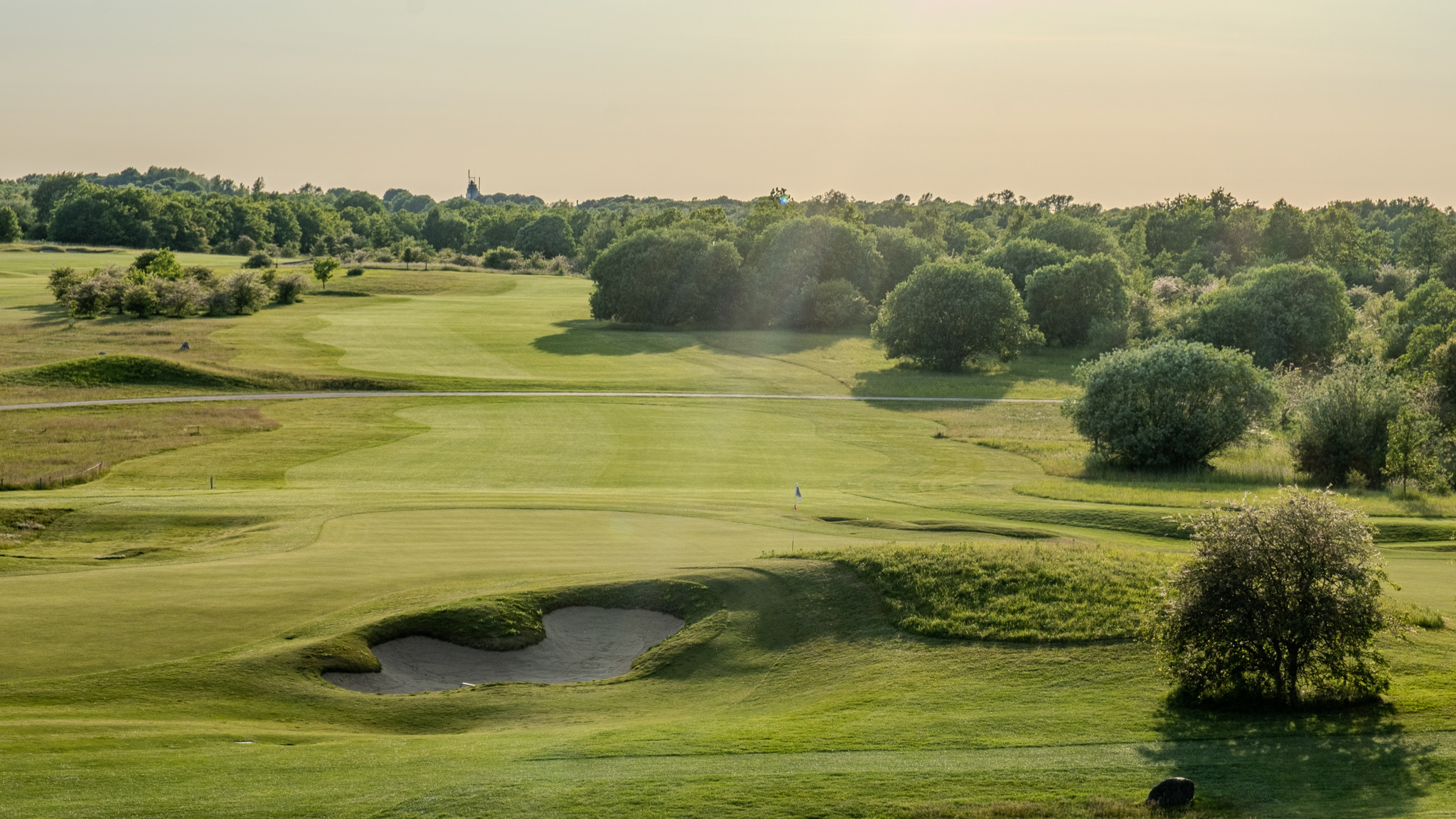 Golf course at Hedeland Golf Club in the evening sun with bunker and green surroundings.