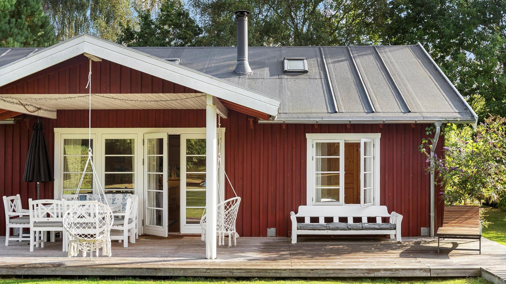 Terrasse ved rødt feriehus med hvide havemøbler.