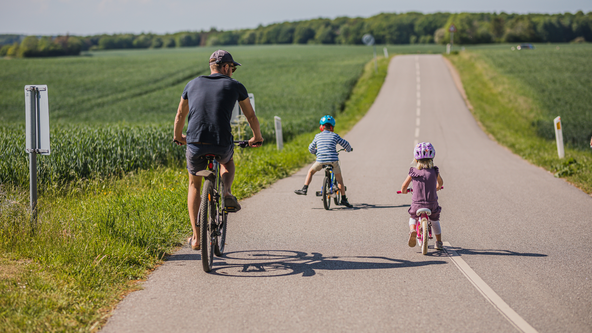Familie på cykeltur ad landevej gennem grønne marker nær Sonnerupgaard Gods.