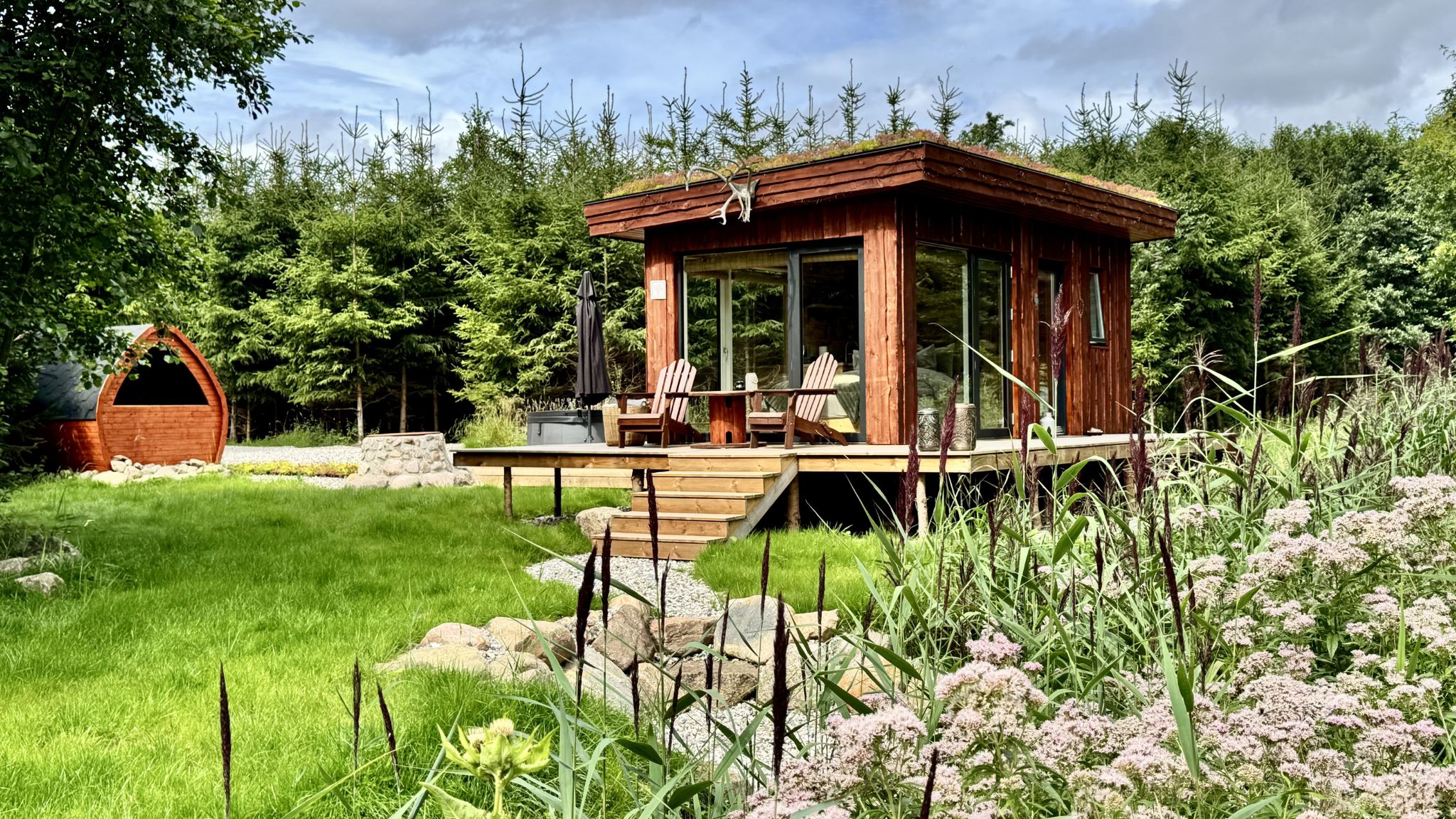 Naturhütte von Heart of Nature mit Terrasse und großen Fenstern in grüner Umgebung.