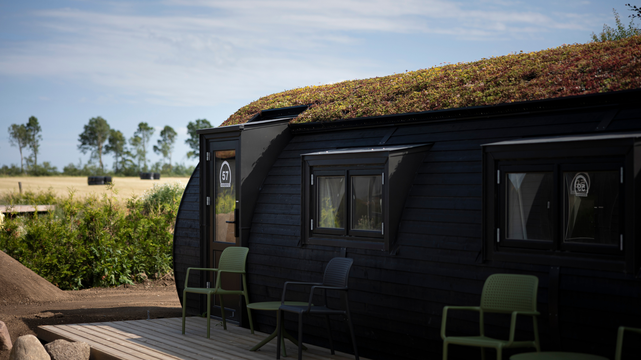 Sort feriehytte med grønt tag og terrasse i naturskønne omgivelser.