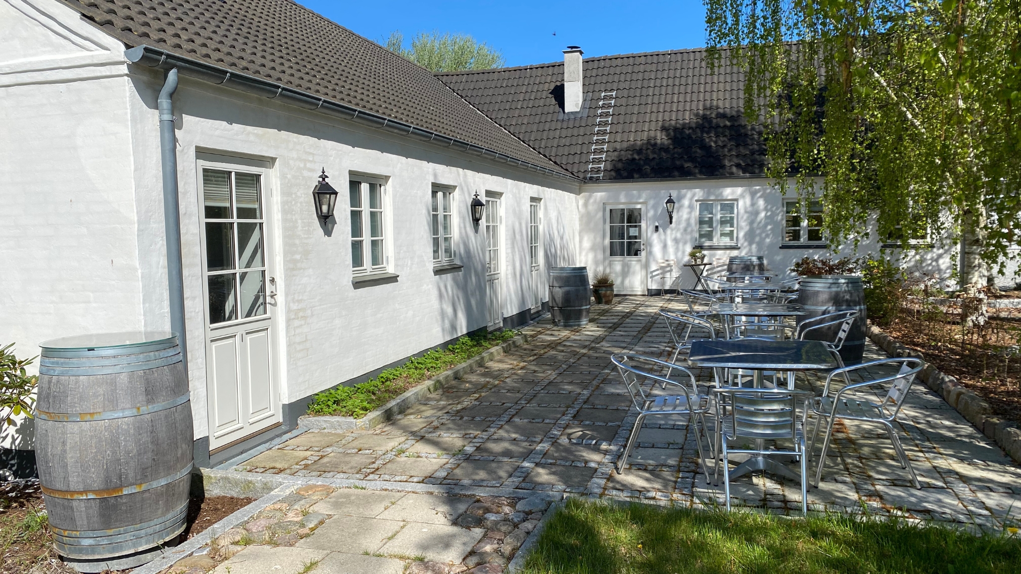 Gemütlicher Innenhof bei LangeLinie Vin mit Tischen, Stühlen und Weinfässern vor weiß getünchten Gebäuden.