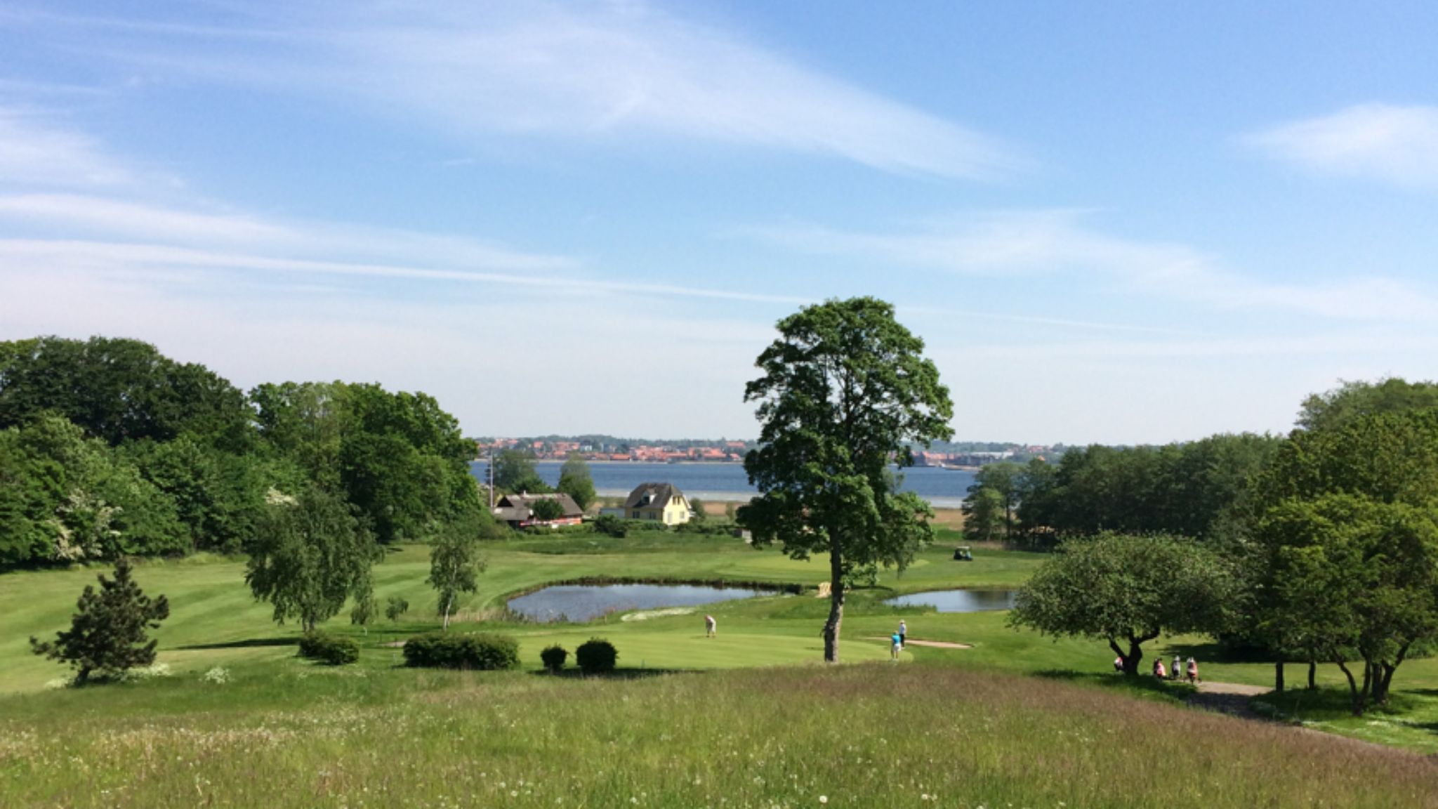 Green golf course at Frederikssund Golf Club with ponds, golfers and views of the fjord.