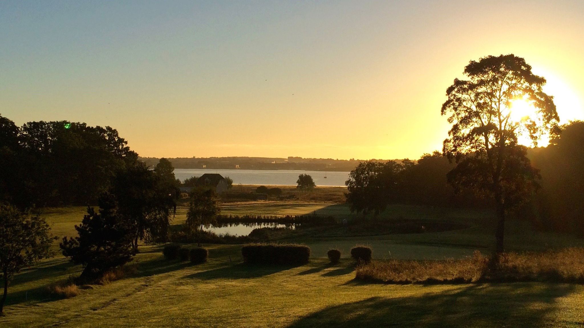 Frederikssund Golf Club golf course with pond and large trees at sunset.
