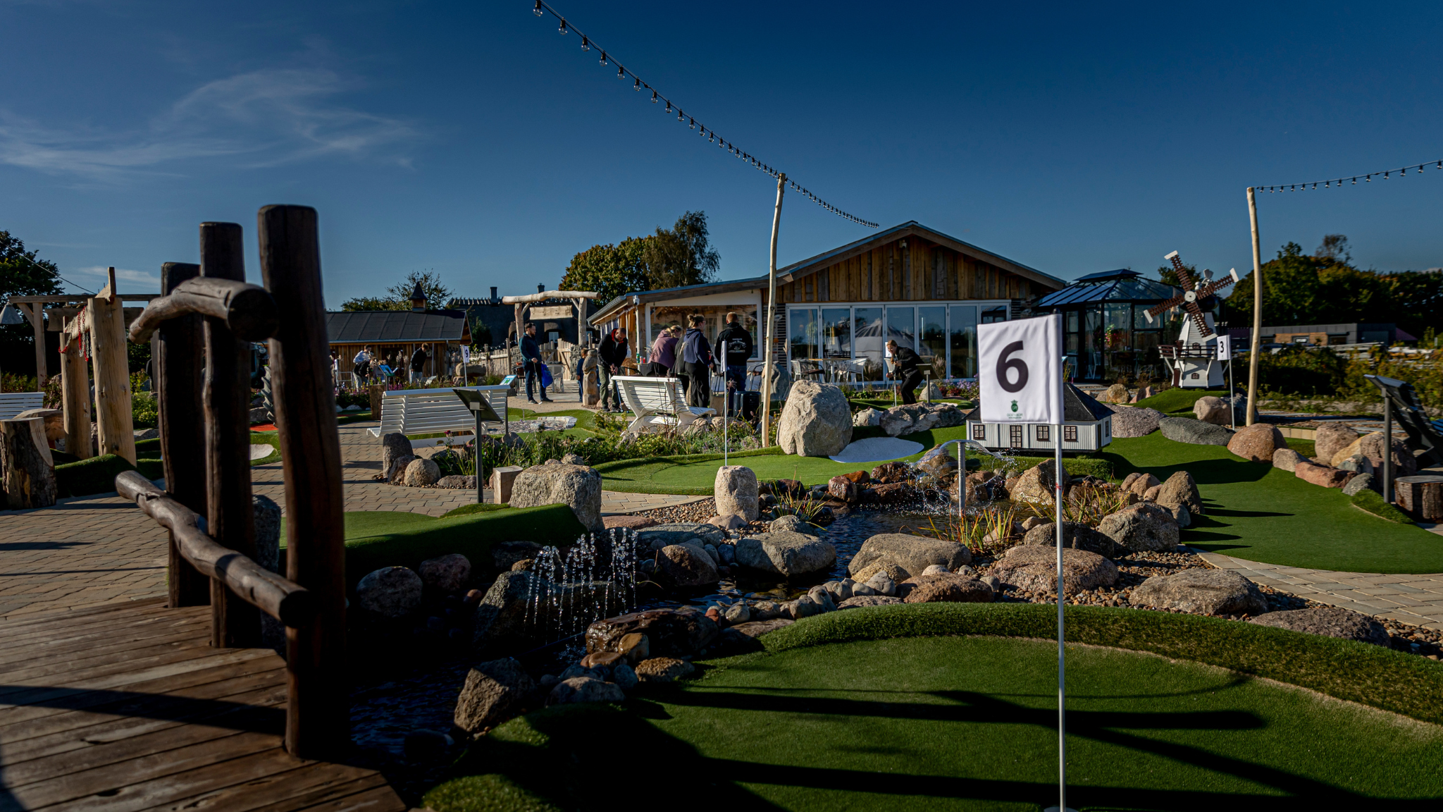 Minigolfanlage bei Countryside Adventure mit Bachlauf, Felsen, Holzbrücke und grünen Bahnen.