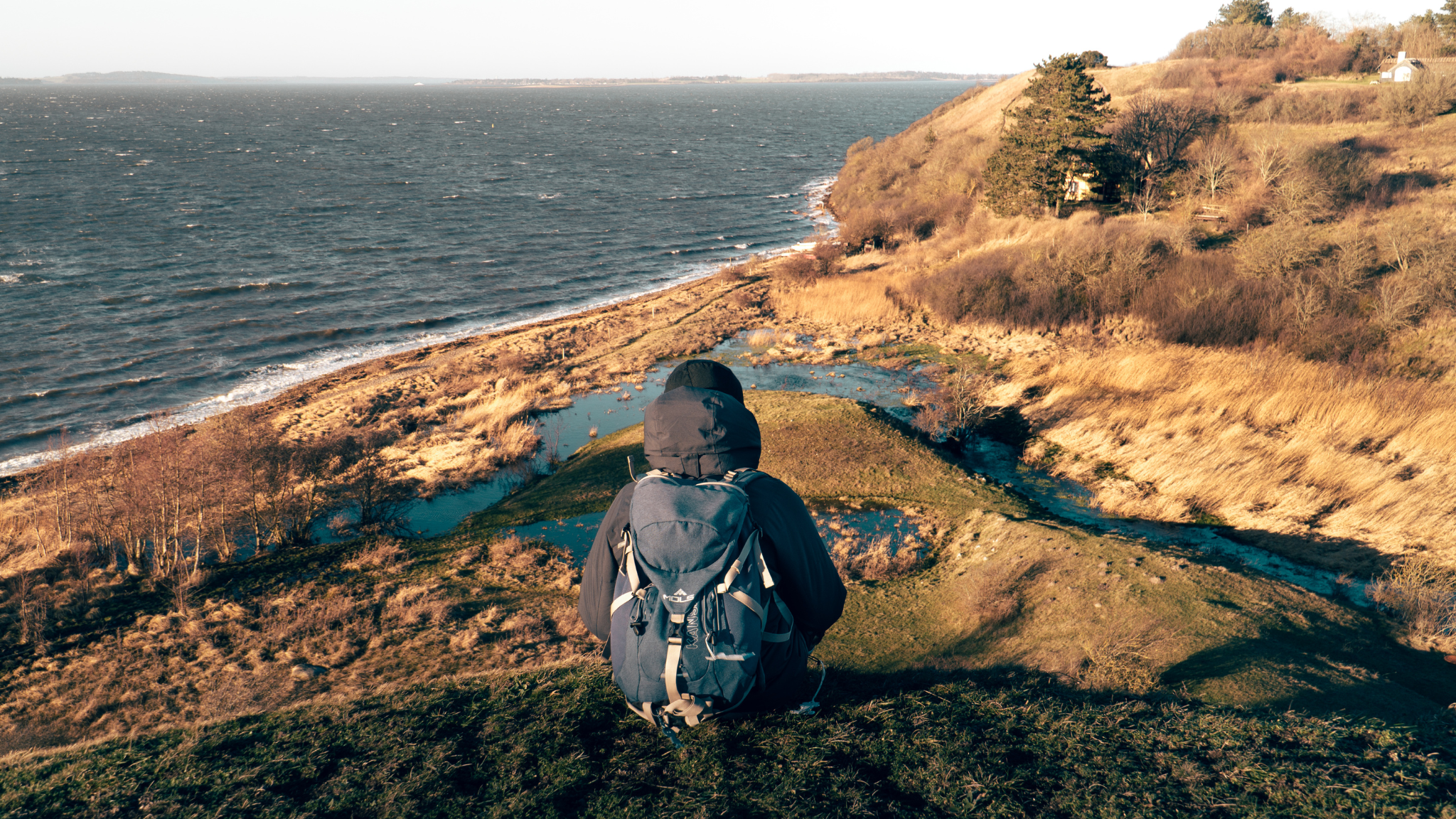 Hiker with backpack in Ejby Ådal overlooking the valley, beach and coast.