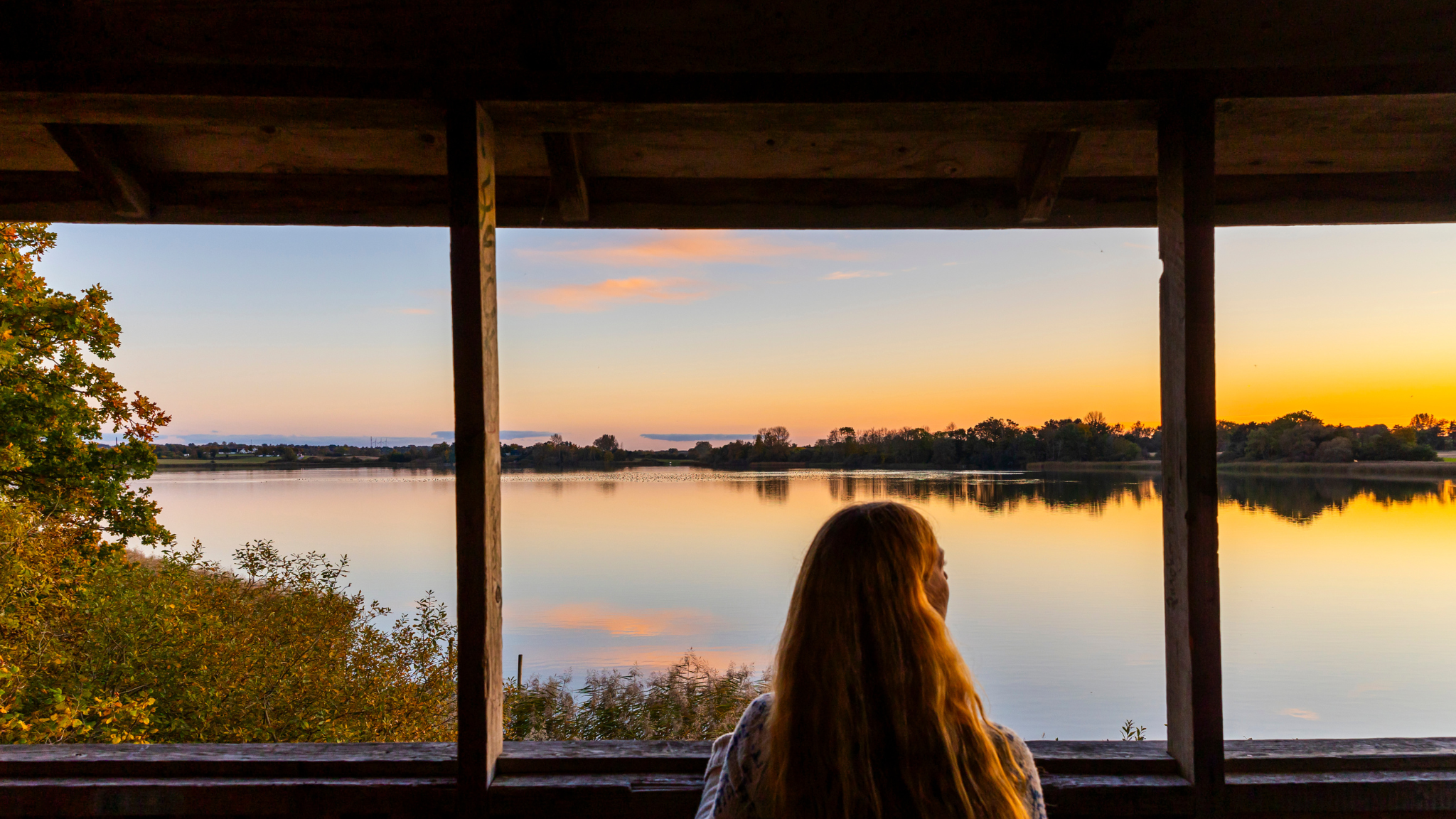 Person at a viewpoint overlooking Store Kattinge Sø in golden sunset light.