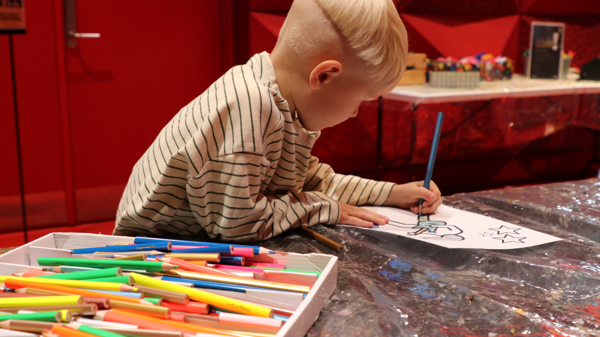 Child drawing with coloured pencils during a creative autumn holiday activity at the rock museum.