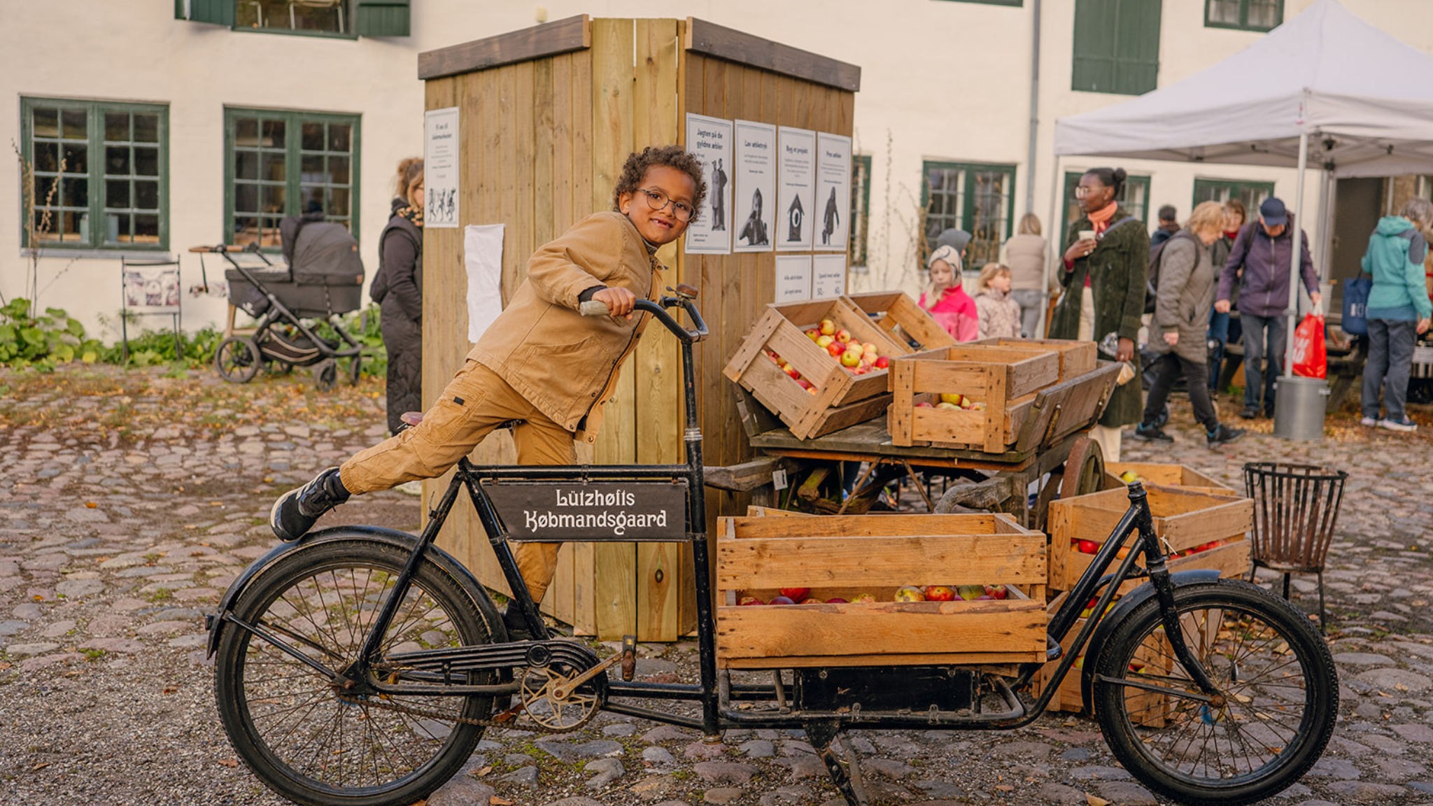 Barn på gammel ladcykel ved æblekasser i gården ved Lützhøfts Købmandsgaard i Roskilde.