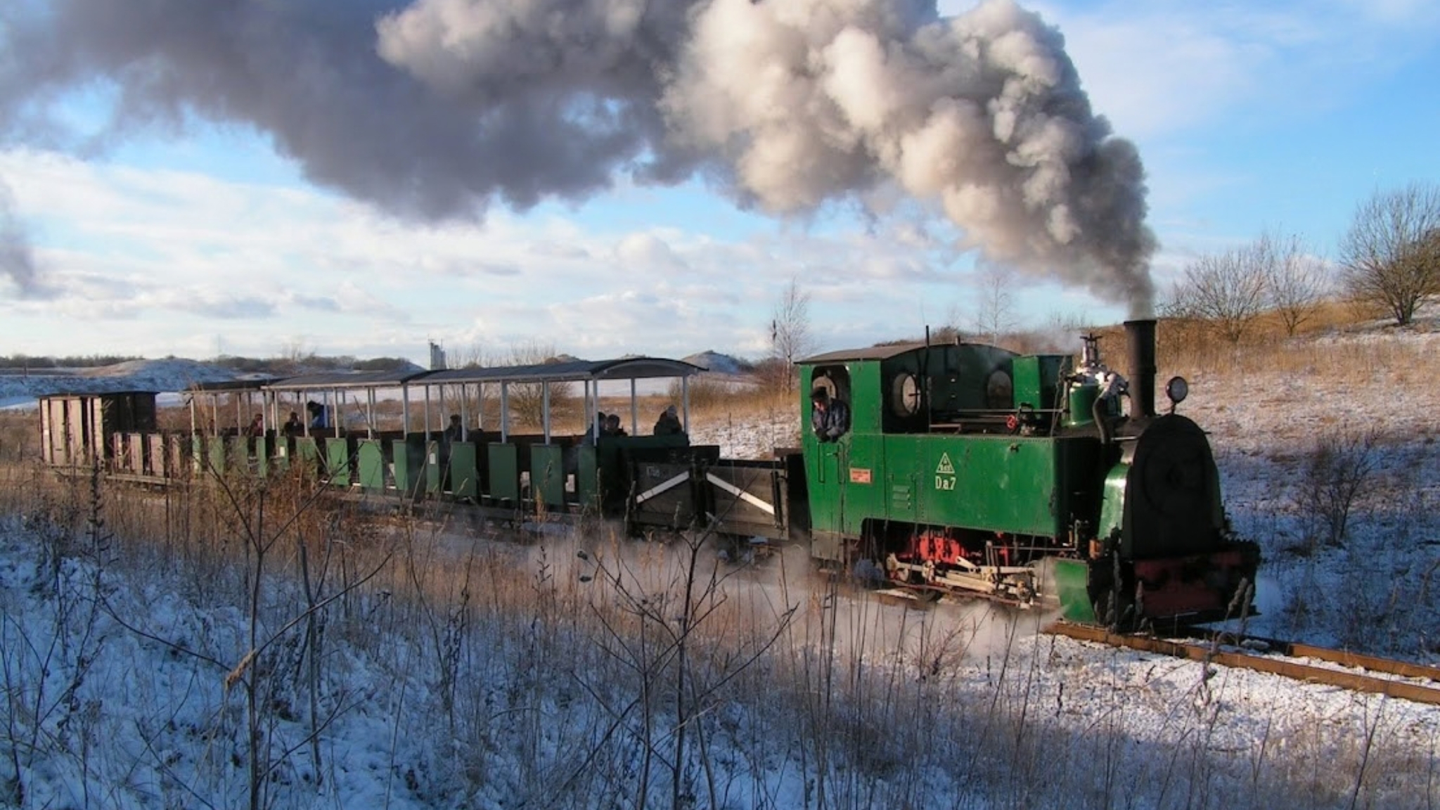 Grüne Dampflokomotive mit Personenwagen fährt durch die Winterlandschaft von Hedeland.