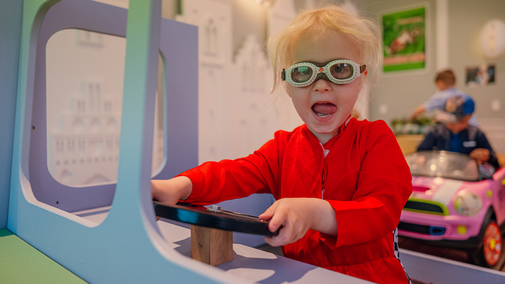 Child wearing driving goggles plays at an interactive car exhibit at Roskilde Museum.