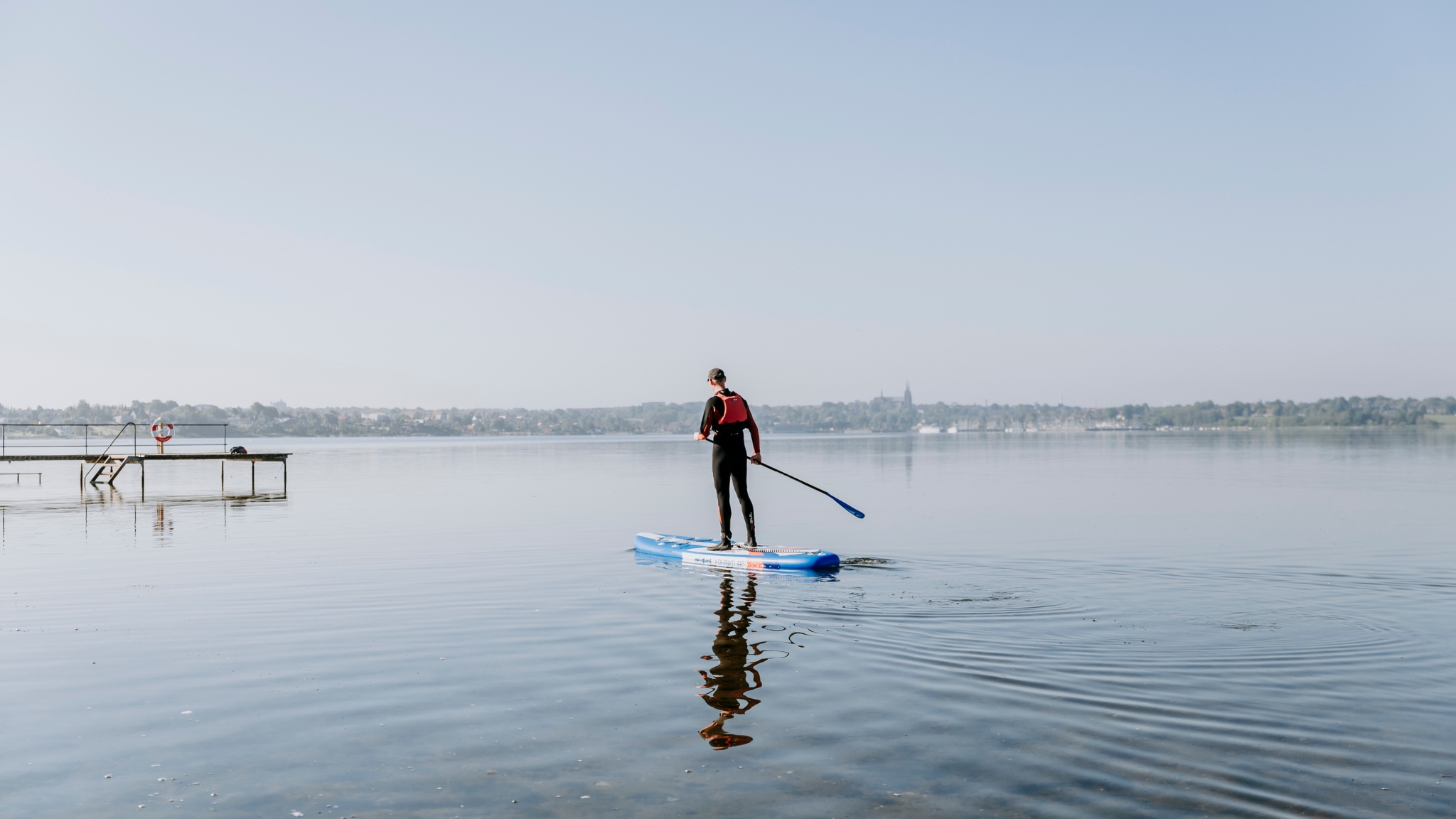 A person on a paddleboard on Roskilde Fjord, with Roskilde Cathedral in the background.