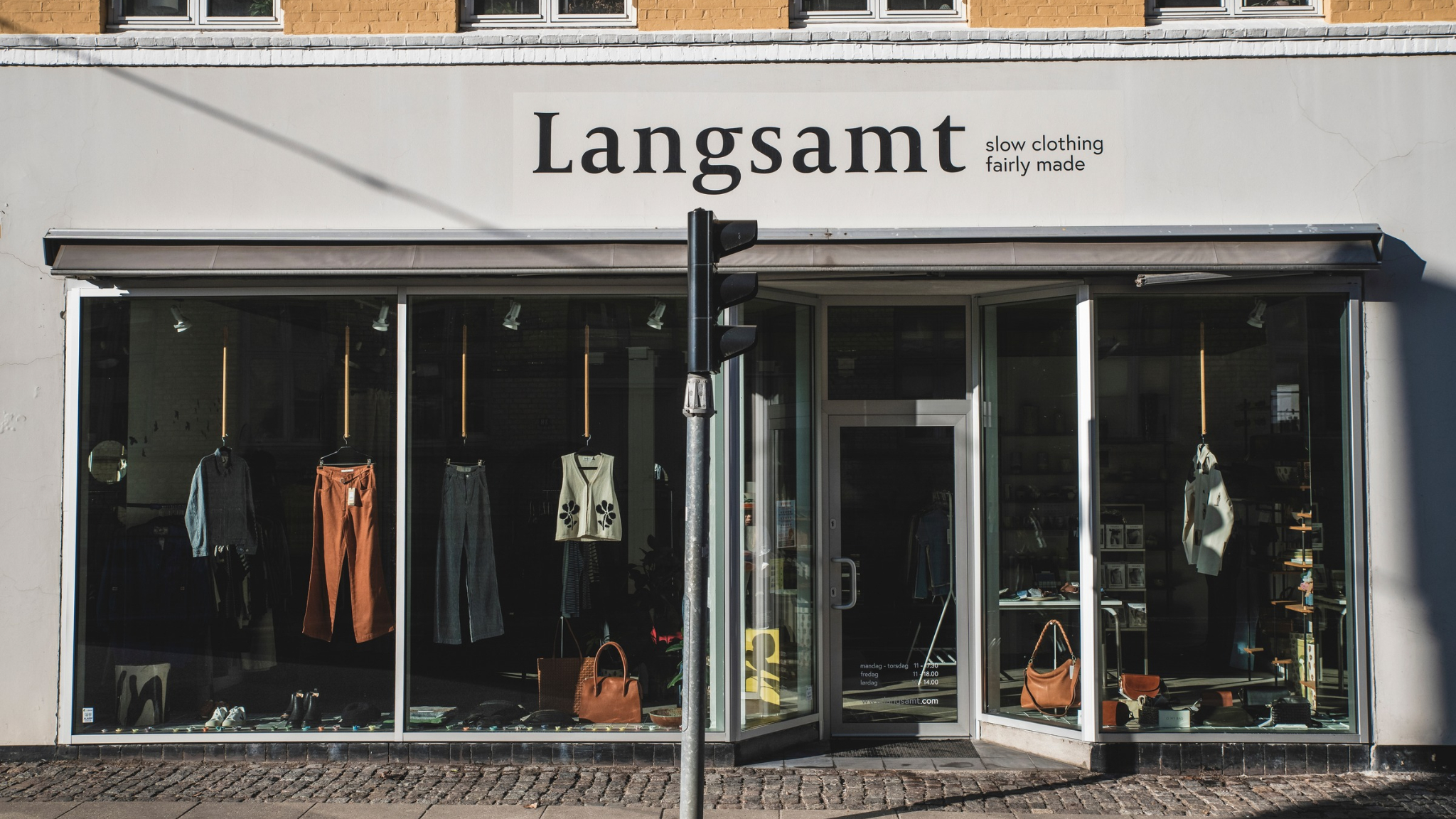 Fassade des Modegeschäfts Langsamt mit großen Schaufenstern, Slow-Fashion-Kleidung, Hosen, Strickmode und Taschen.