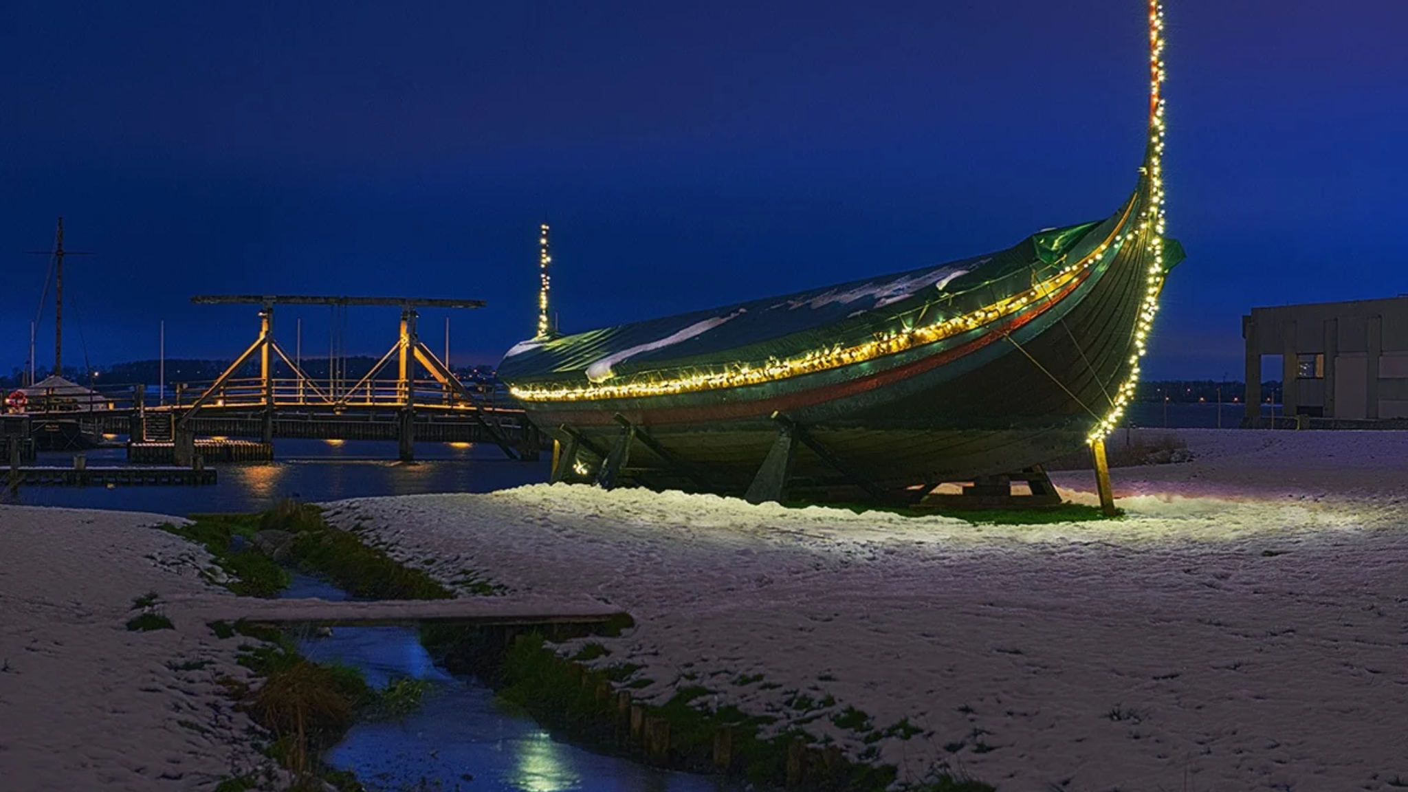 Mit Weihnachtslichtern geschmücktes Wikingerschiff am Wikingerschiffsmuseum in Roskilde an einem verschneiten Winterabend.