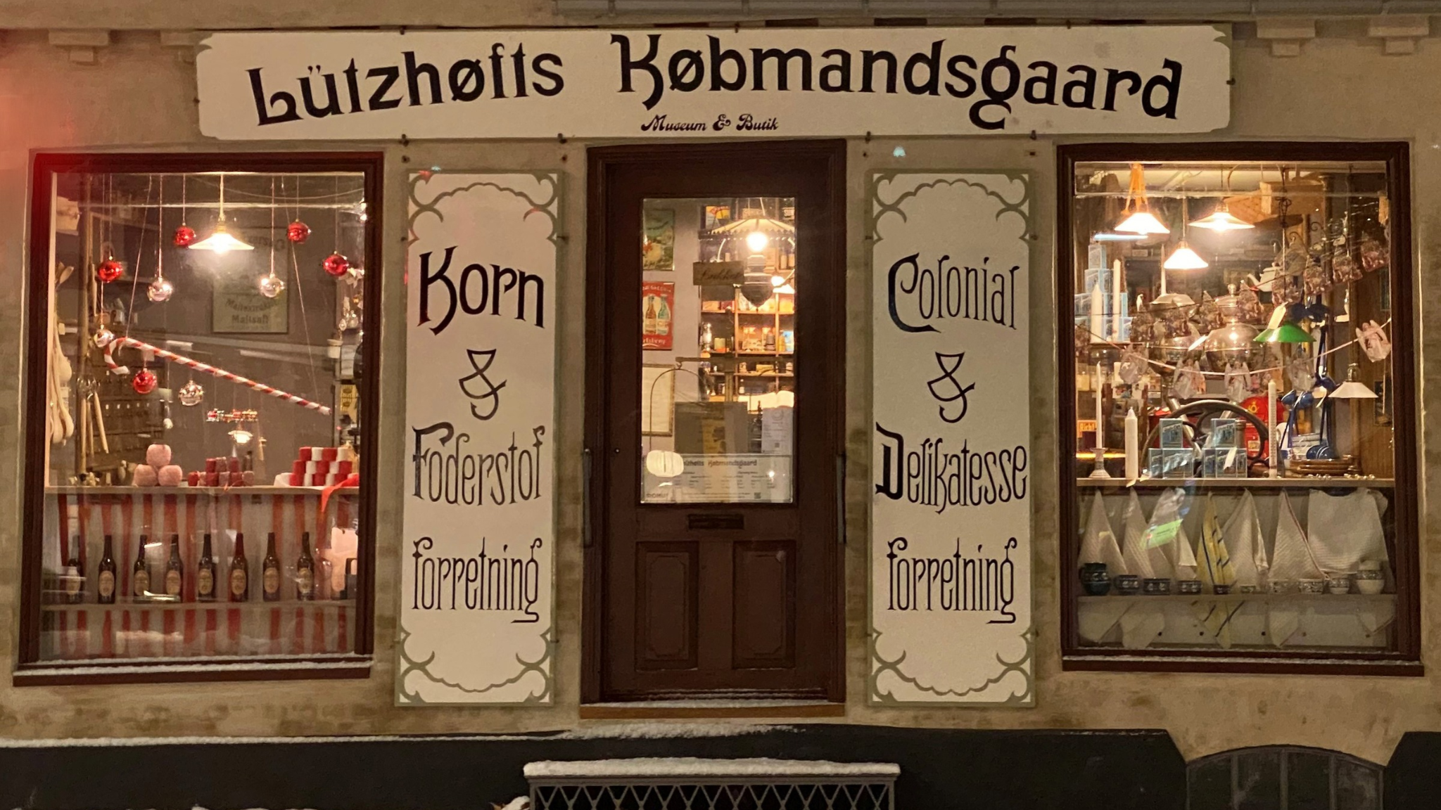 Historische Fassade von Lützhøfts Købmandsgård in Roskilde mit beleuchteten Schaufenstern und nostalgischen Schildern.