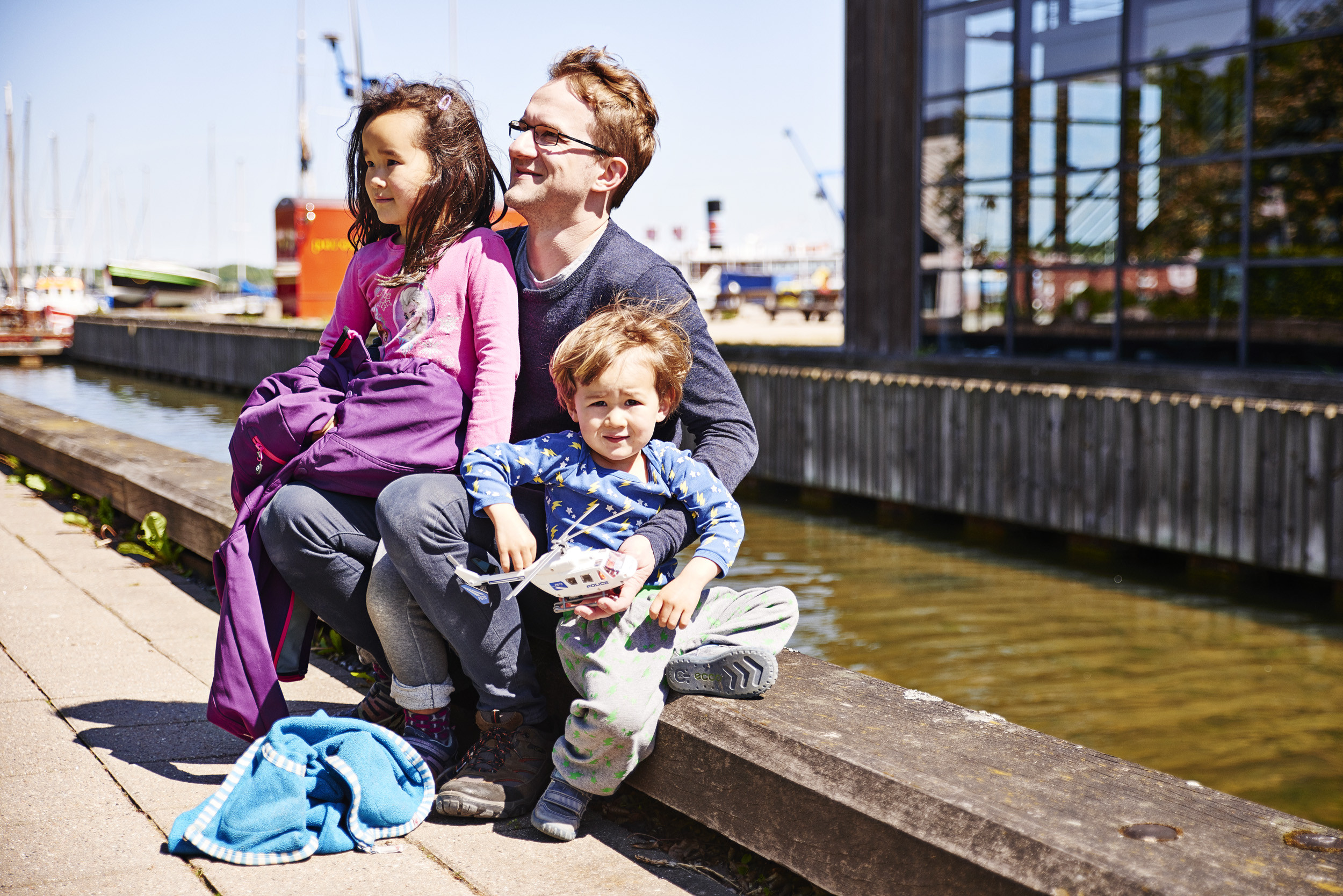 An adult and two children sitting on the quay at Roskilde Harbour