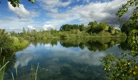 Der See in der ehemaligen Kiesgrube Skuldelev unter blauem Himmel mit Wolken.